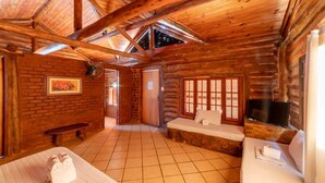 A log cabin room with a high ceiling, a fireplace, a bed, a bench, and a TV. - Hotel Fazenda Santa Helena (Simao Pereira)
