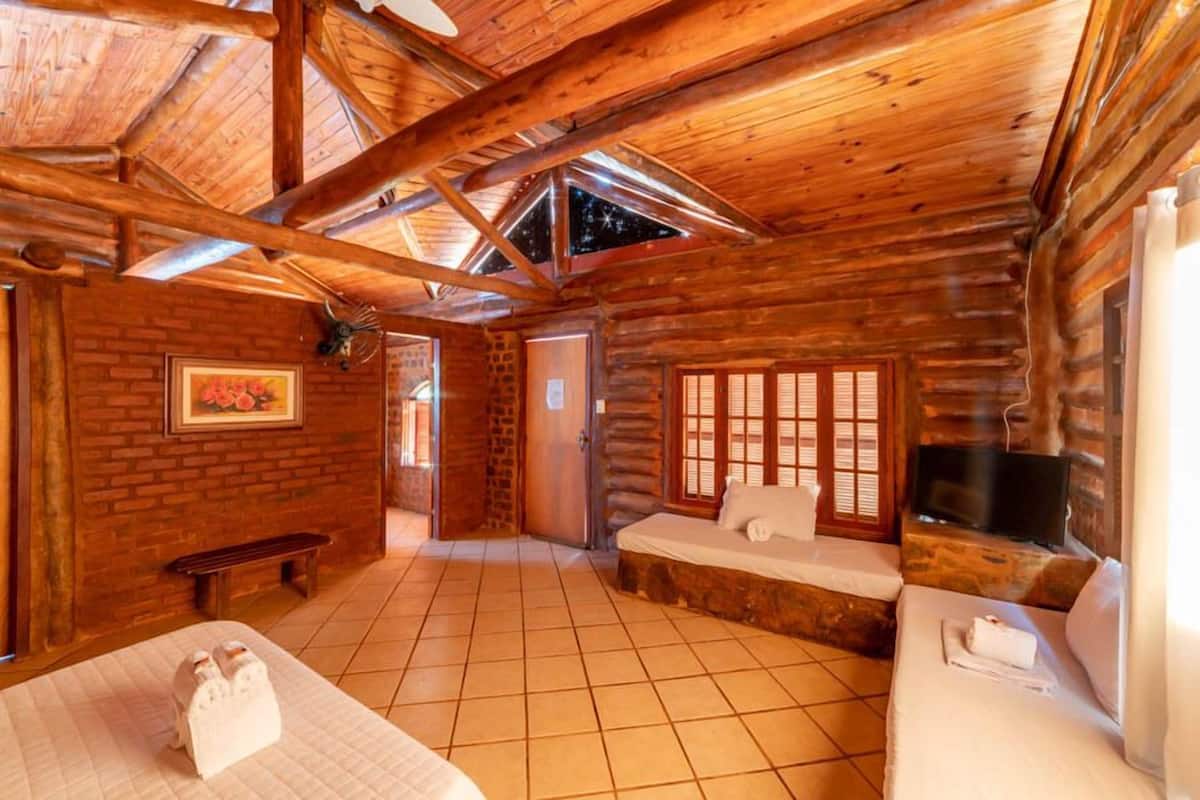 A log cabin room with a high ceiling, a fireplace, a bed, a bench, and a TV.