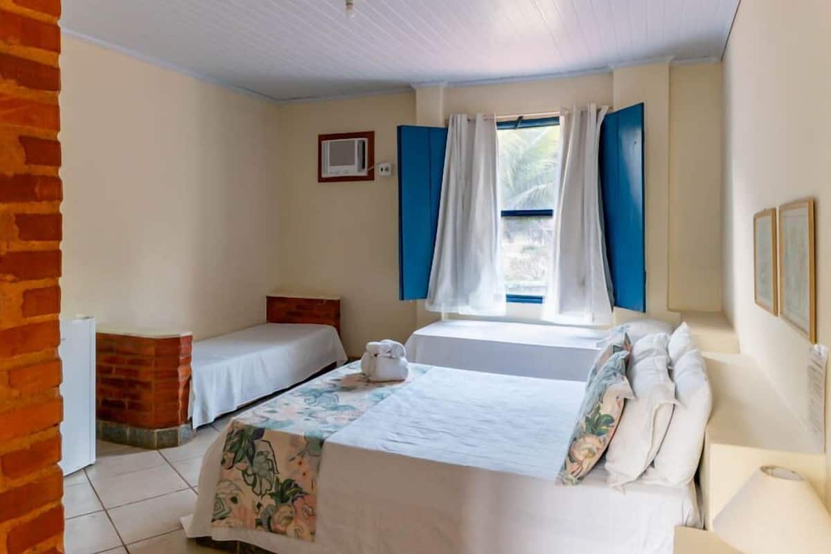 A room with two beds, a window with blue curtains, a brick wall, and a small white radiator.