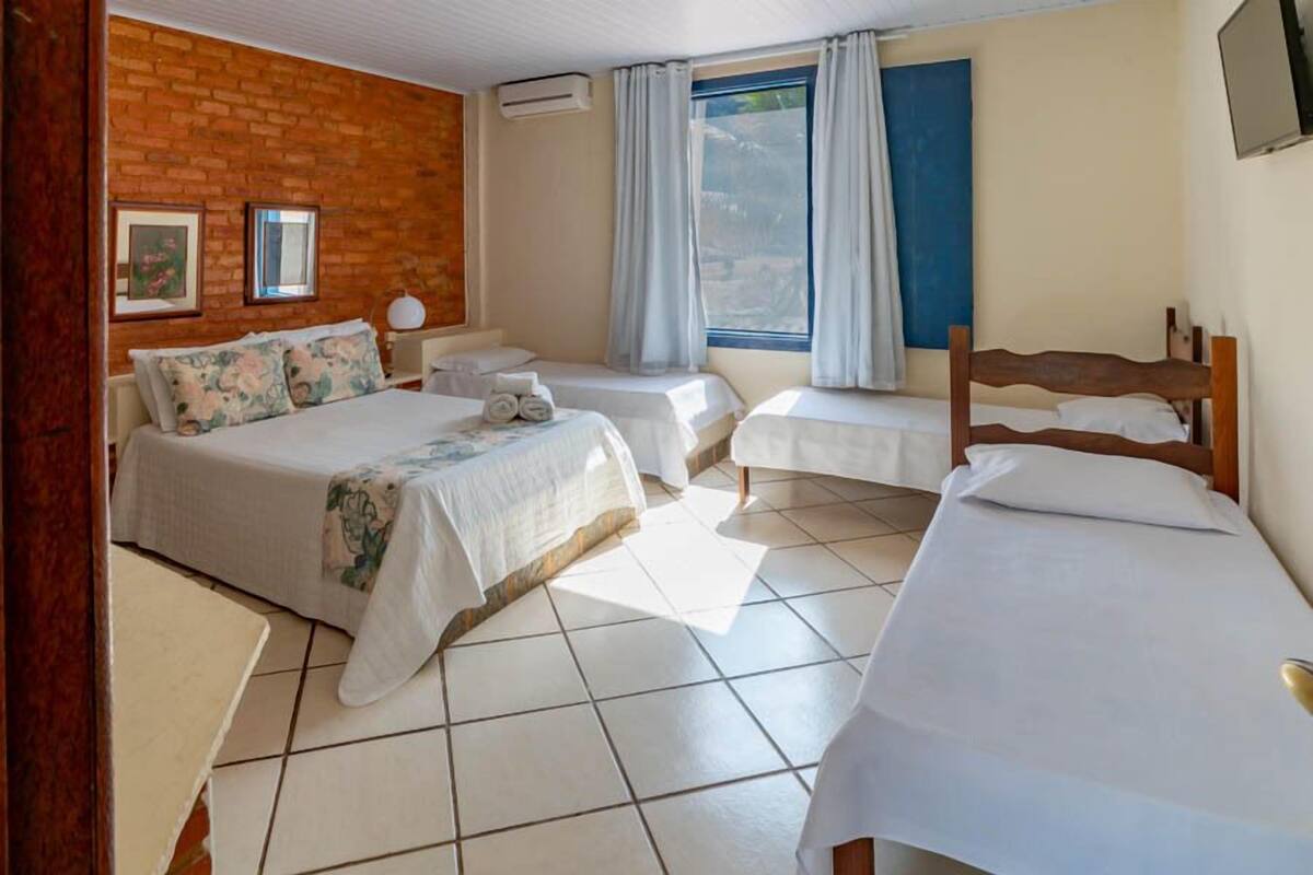 A hotel room with three beds, a brick wall, a window with curtains, and a tiled floor.