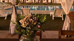 A poolside area with a clear view of the pool, lounge chairs, and a decorative vase with flowers. - Hotel Fazenda Santa Helena (Simao Pereira)