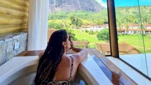 A woman in a bathtub with a view of a mountain and greenery. - Hotel Fazenda Santa Helena (Simao Pereira)