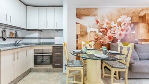Una cocina moderna con armarios blancos, horno empotrado y comedor con mesa y sillas de vidrio.