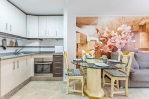 Una cocina moderna con armarios blancos, horno empotrado y comedor con mesa y sillas de vidrio.