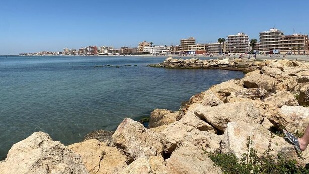 Un paisaje urbano costero con costa rocosa, cielo azul despejado y edificios a lo largo de la costa.