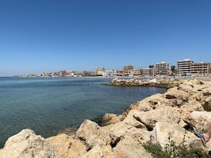Un paisaje urbano costero con costa rocosa, cielo azul despejado y edificios a lo largo de la costa.