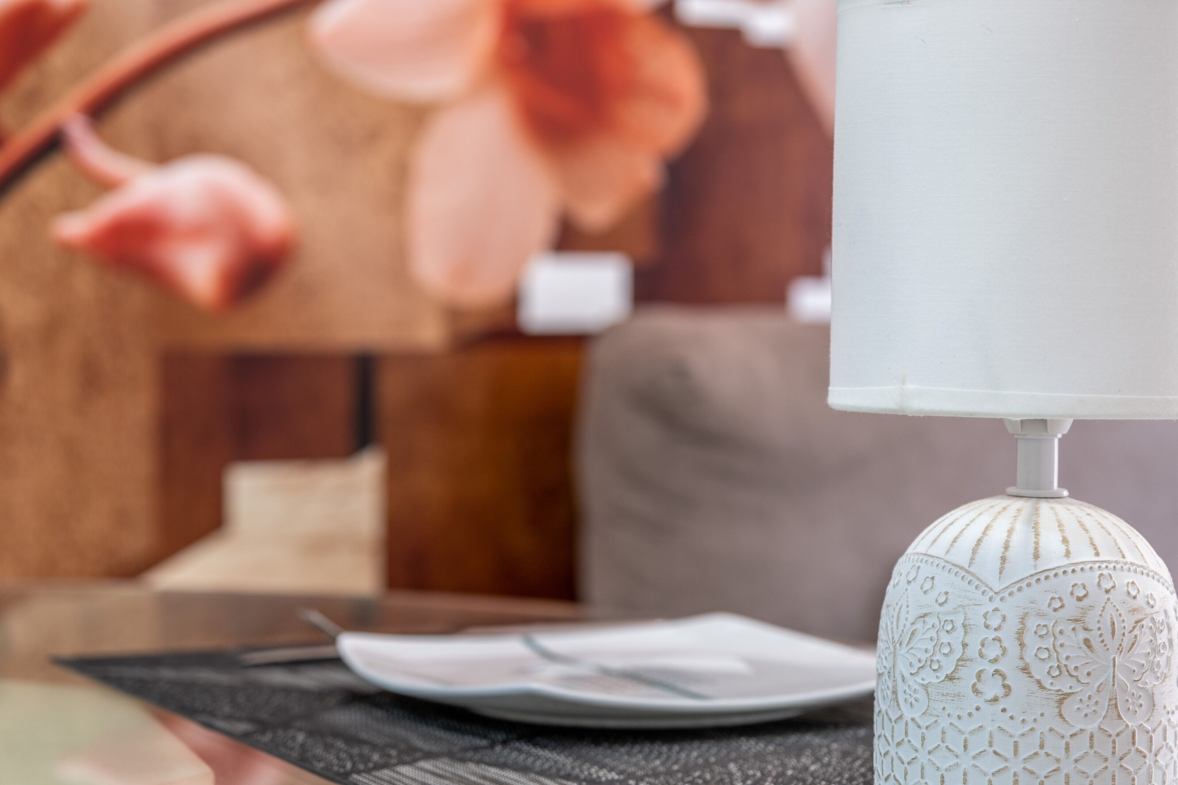 A table with a white tablecloth, a plate, and a white lamp with intricate patterns.