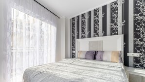 Un dormitorio con una cama grande, cabecera y una ventana con cortinas traslúcidas.