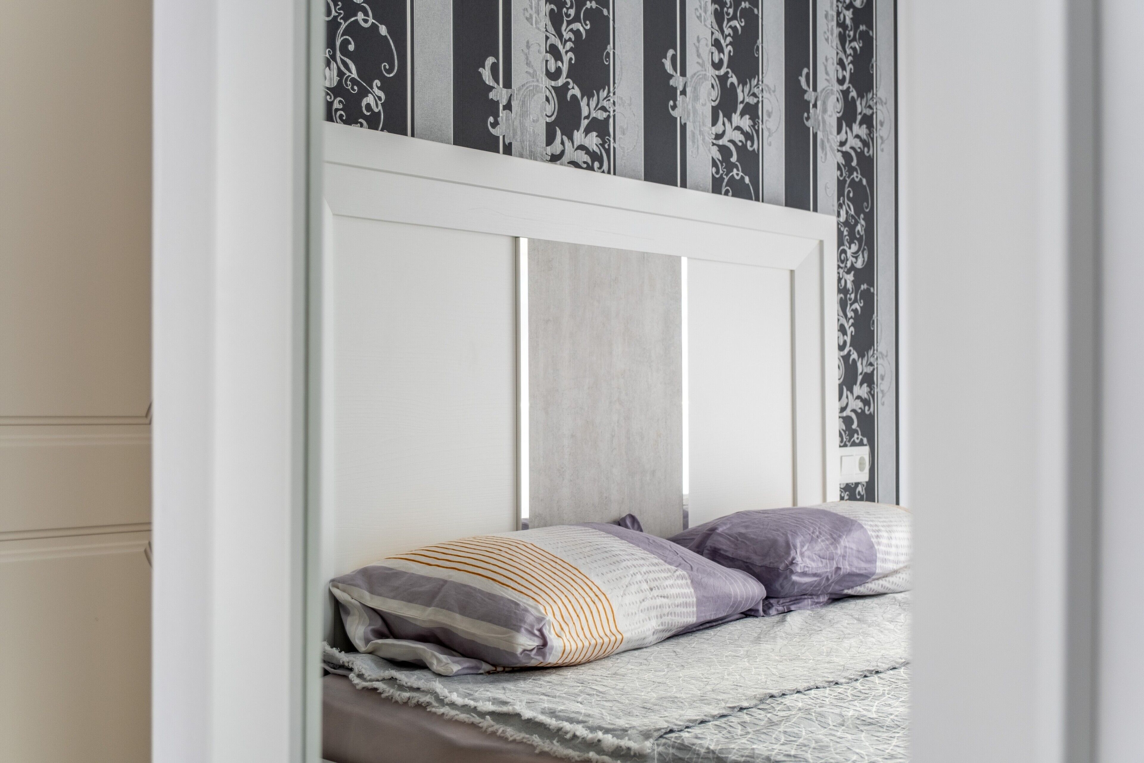 Un dormitorio con un cabecero blanco, una cama con cabecero a rayas grises y blancas, y dos almohadas.