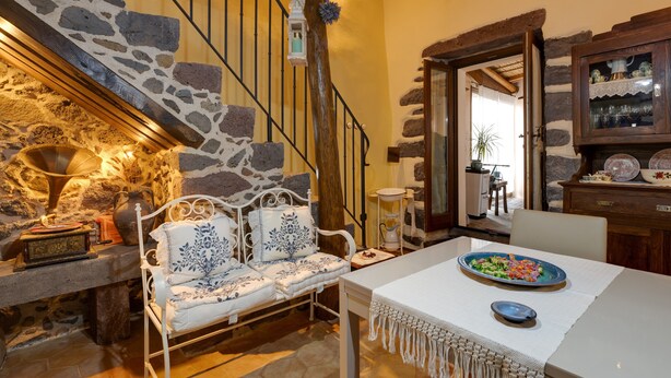 Un escalier en pierre, un banc blanc rembourré, une table avec une assiette de nourriture et un buffet en bois contenant de la verrerie.