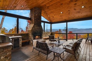 An outdoor deck with a stone fireplace, seating, and a view of autumn foliage and mountains. - Luxury 10BR/12BA Cabin w/Indoor Pool, 2 Hot Tubs, Arcade, & Theater! Mountain Views! (Sevierville)