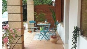 Un patio cubierto con suelo de baldosas, una mesa con sillas y plantas en macetas.