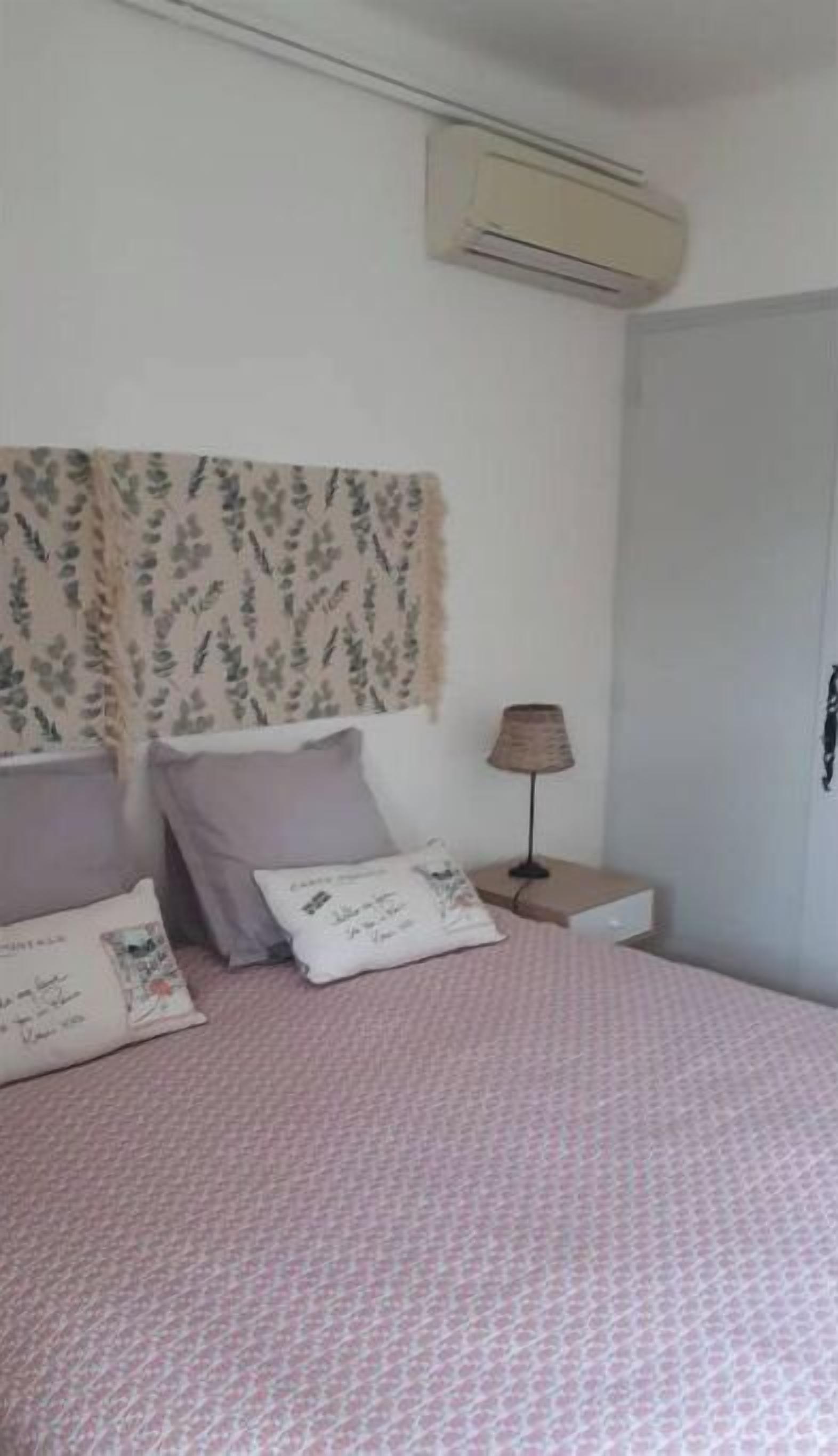 A bedroom with a bed, pillows, a lamp, and an air conditioning unit.