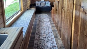 A cabin interior with a wooden ceiling, a ceiling fan, a window, a couch, a rug, and a sign that reads "grateful".