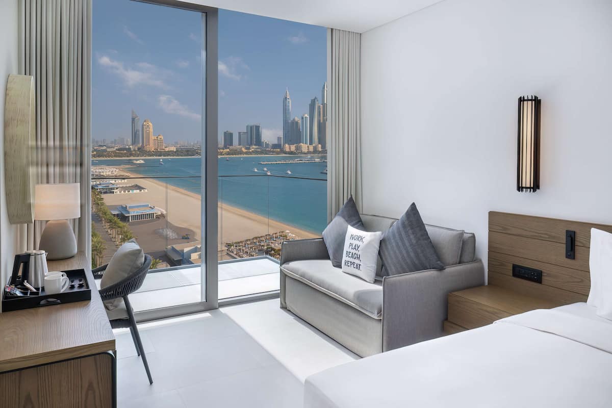 A modern hotel room with a large window offering a view of a city skyline and beach.