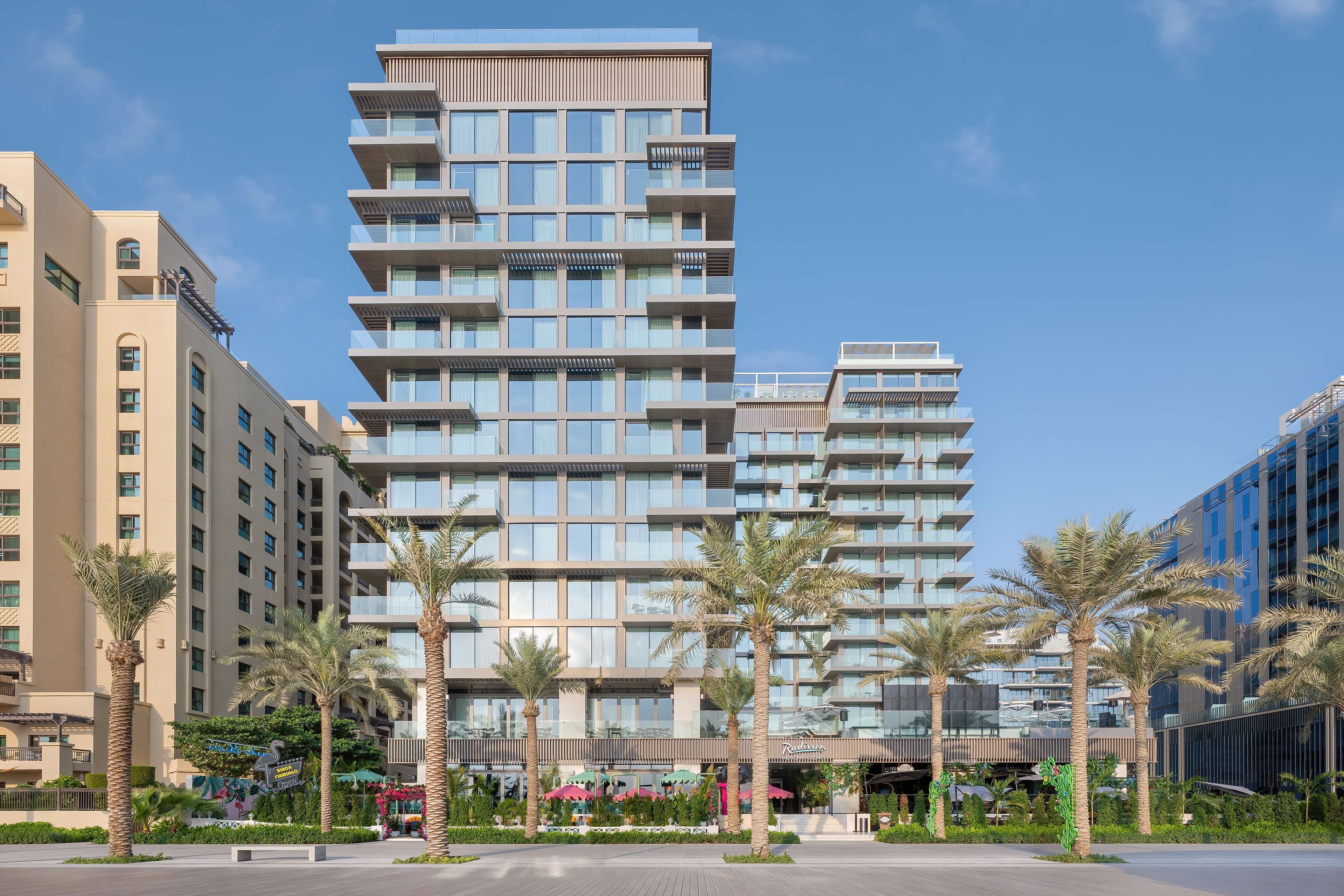 A multi-story hotel with balconies, palm trees, and a landscaped area.