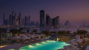 A rooftop pool with lounge chairs and umbrellas, overlooking a city skyline and a body of water. - Radisson Beach Resort Palm Jumeirah (Dubai)