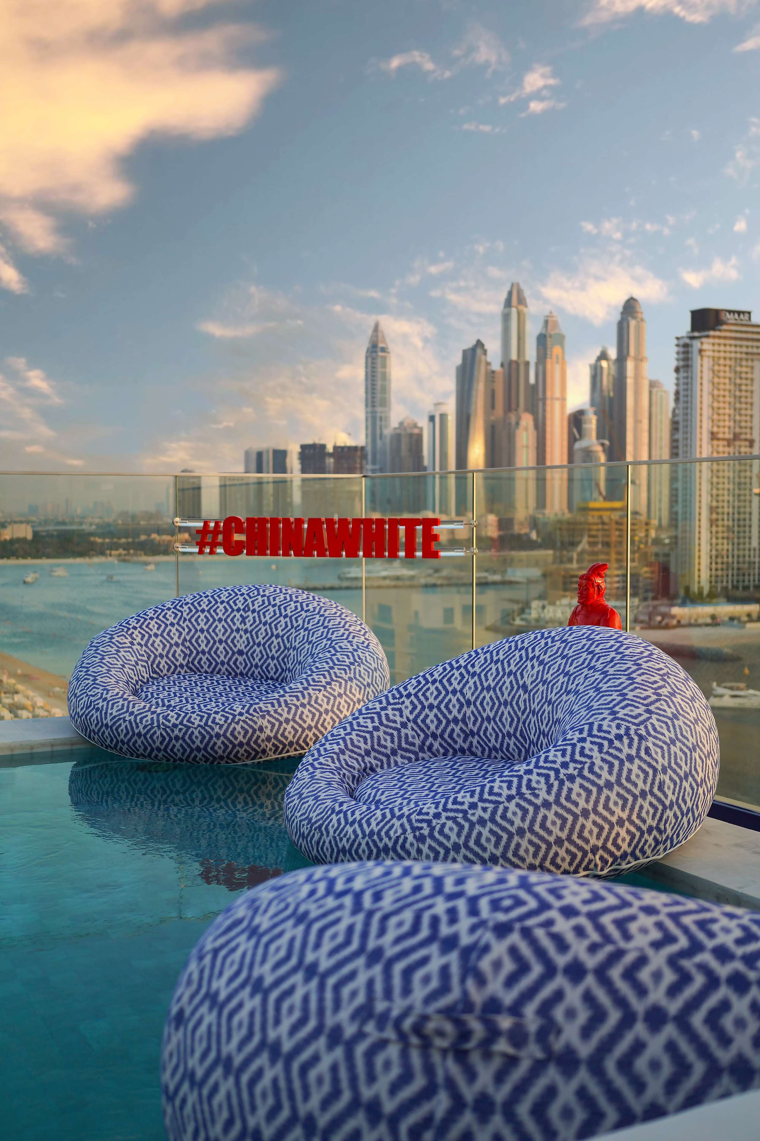 Zona de piscina en la azotea con sillones orejeros estampados y vistas al horizonte de la ciudad.