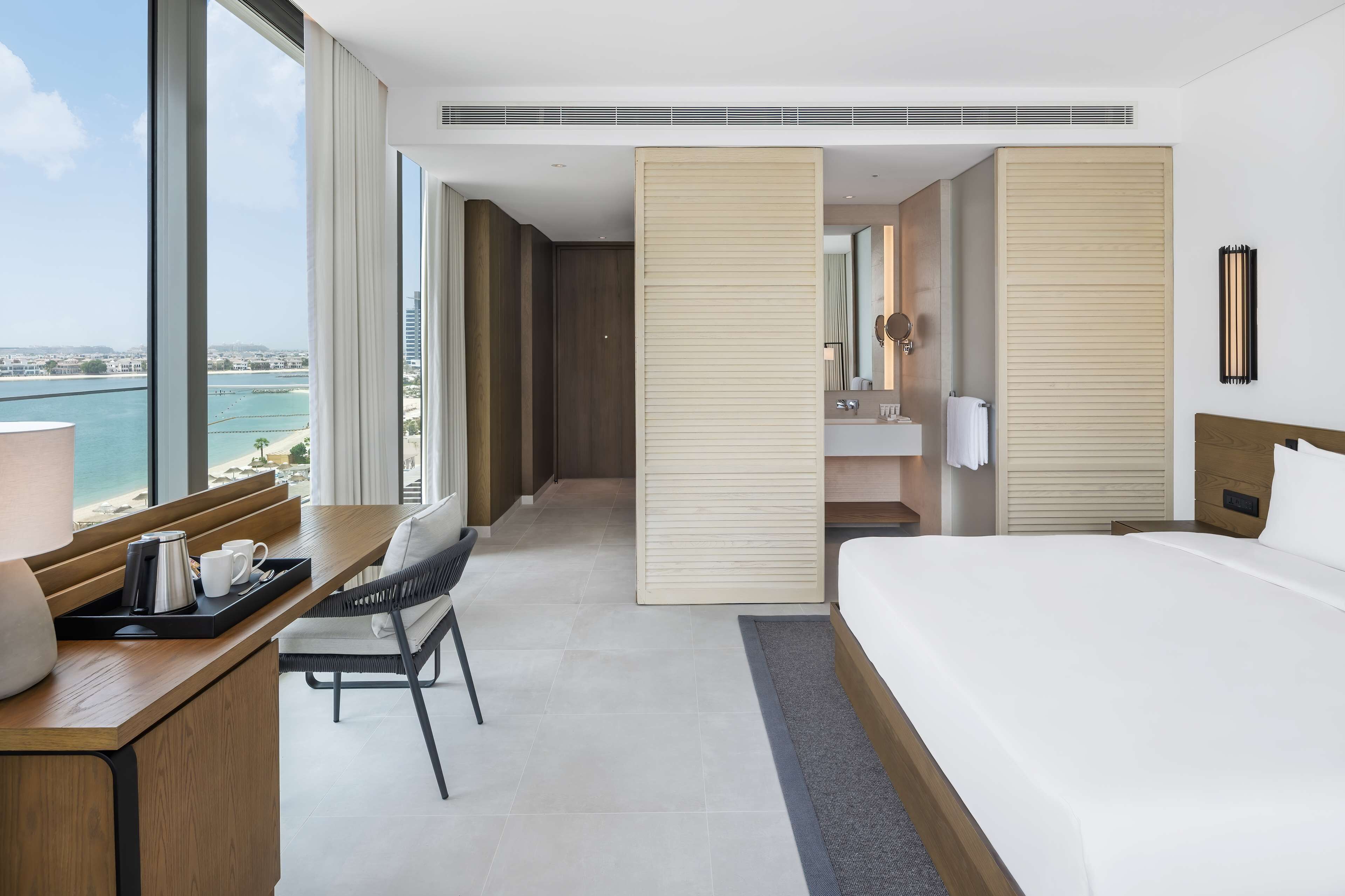 Een moderne hotelkamer met een groot bed, een bureau met koffiezetapparaat en uitzicht op zee.