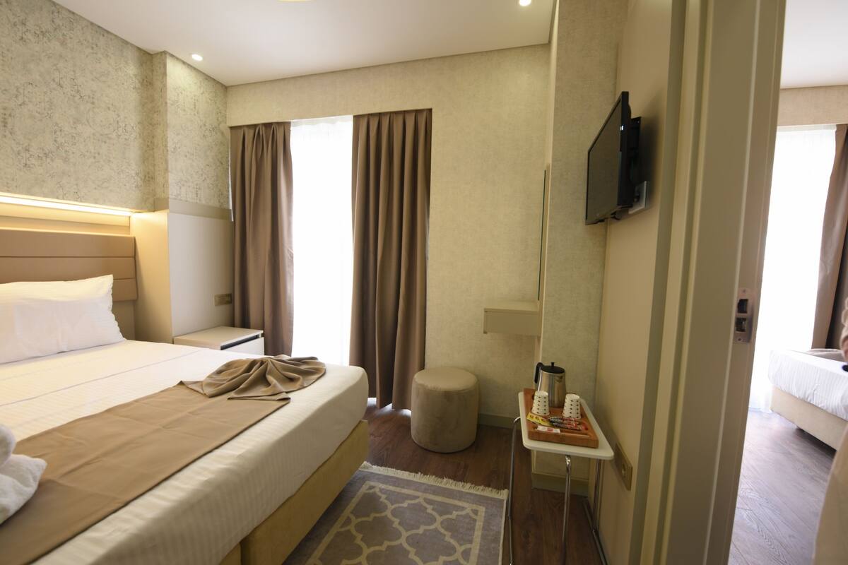 A hotel room with a bed, bedside table, TV, and a small stool.