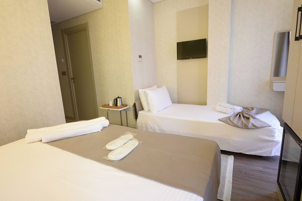 A hotel room with two beds, a small table with a coffee maker, a TV mounted on the wall, and a door leading to another room.
