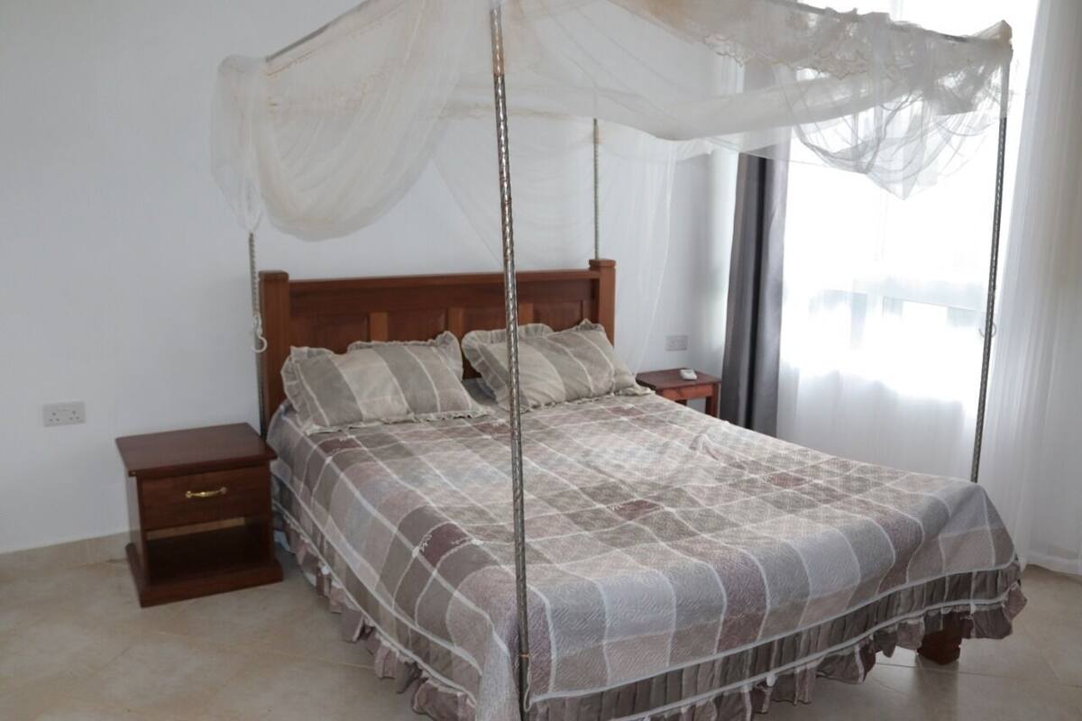 A bedroom with a four-poster bed, a nightstand, and a window with curtains.