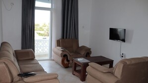 A living room with a sofa, armchair, and a TV on the wall. - Stay.Plus Kijani Apartments (Malindi)