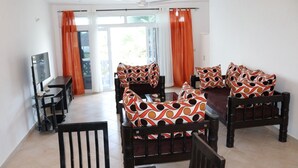 A living room with a sofa set, a TV, and a dining table. - Stay.Plus Kijani Apartments (Malindi)