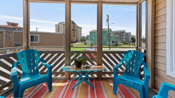 Varanda com duas cadeiras turquesa e uma mesa pequena, com vista para uma área residencial com edifícios e uma rua.