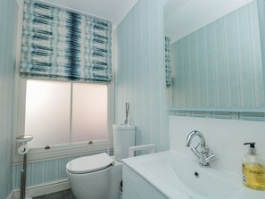 Une salle de bain équipée de toilettes, d’un lavabo et d’une fenêtre agrémentée de rideaux à motifs.