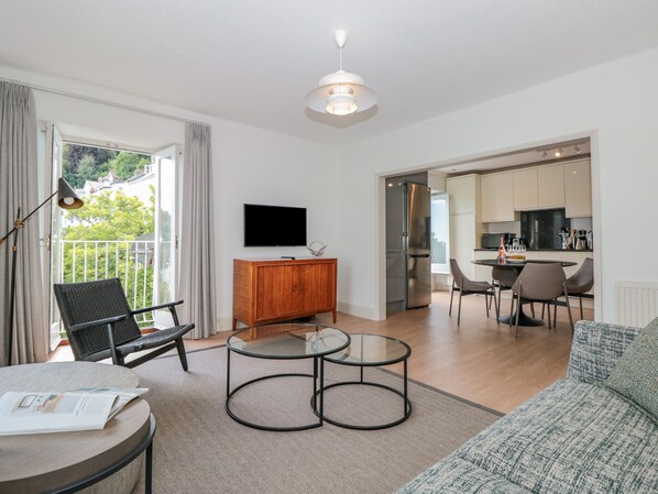 A modern living room with a sofa, a coffee table, a TV, and a dining area with chairs and a table.