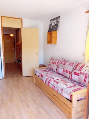 A cozy room with a wooden bed, a small wooden cabinet, and a door leading to another room.