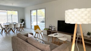 Een moderne woonkamer met een grote bank, een eethoek met stoelen, een televisie en een bijzondere lamp.
