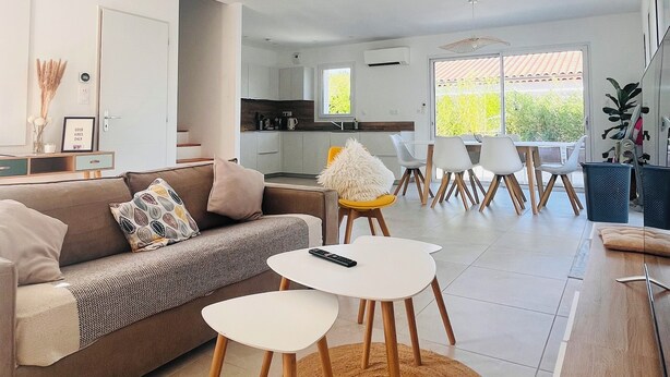 Een moderne woonkamer met een bank, twee witte tafels en een eethoek met stoelen.