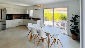 Een moderne keuken met witte kasten, een eethoek met een witte tafel en stoelen, en een grote schuifdeur die uitkomt op een terras.