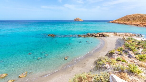 Een kustlandschap met helder turquoise water, een zandstrand en rotsachtige rotsformaties.