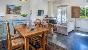 Een gezellig eetgedeelte met een houten tafel en stoelen, een open haard en uitzicht op groen.