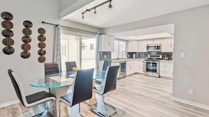 A modern kitchen with stainless steel appliances, a dining area with glass tables and chairs, and a large window providing natural light. - Luxury Vacation Home in Phoenix - Pool - Sleeps 17 (Phoenix)