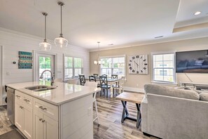 A modern kitchen with a central island, pendant lighting, and a dining area with a view. - Charming Pawleys Island Home ~ 4 Mi to Beach! (Pawleys Island)