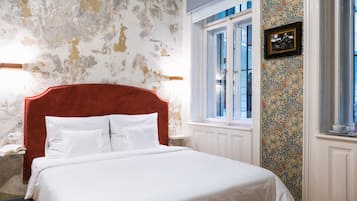 A bed with a red headboard, white bedding, and a wall with peeling paint.