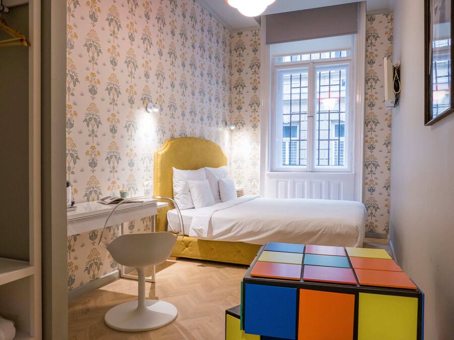Un dormitorio con cama, escritorio, silla y un colorido rompecabezas cúbico en el suelo.