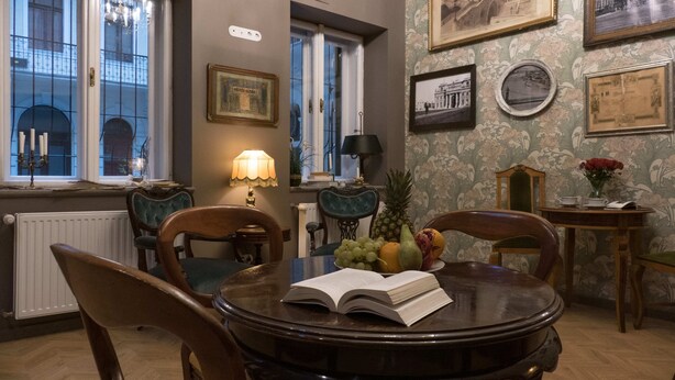 A dining area with a round table, chairs, a book, fruit, and framed pictures on the wall. - Metropolis Budapest Boutique Hotel (Budapest)