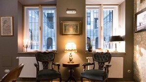 A room with two chairs, a table with a lamp, and a window with a view of buildings. - Metropolis Budapest Boutique Hotel (Budapest)
