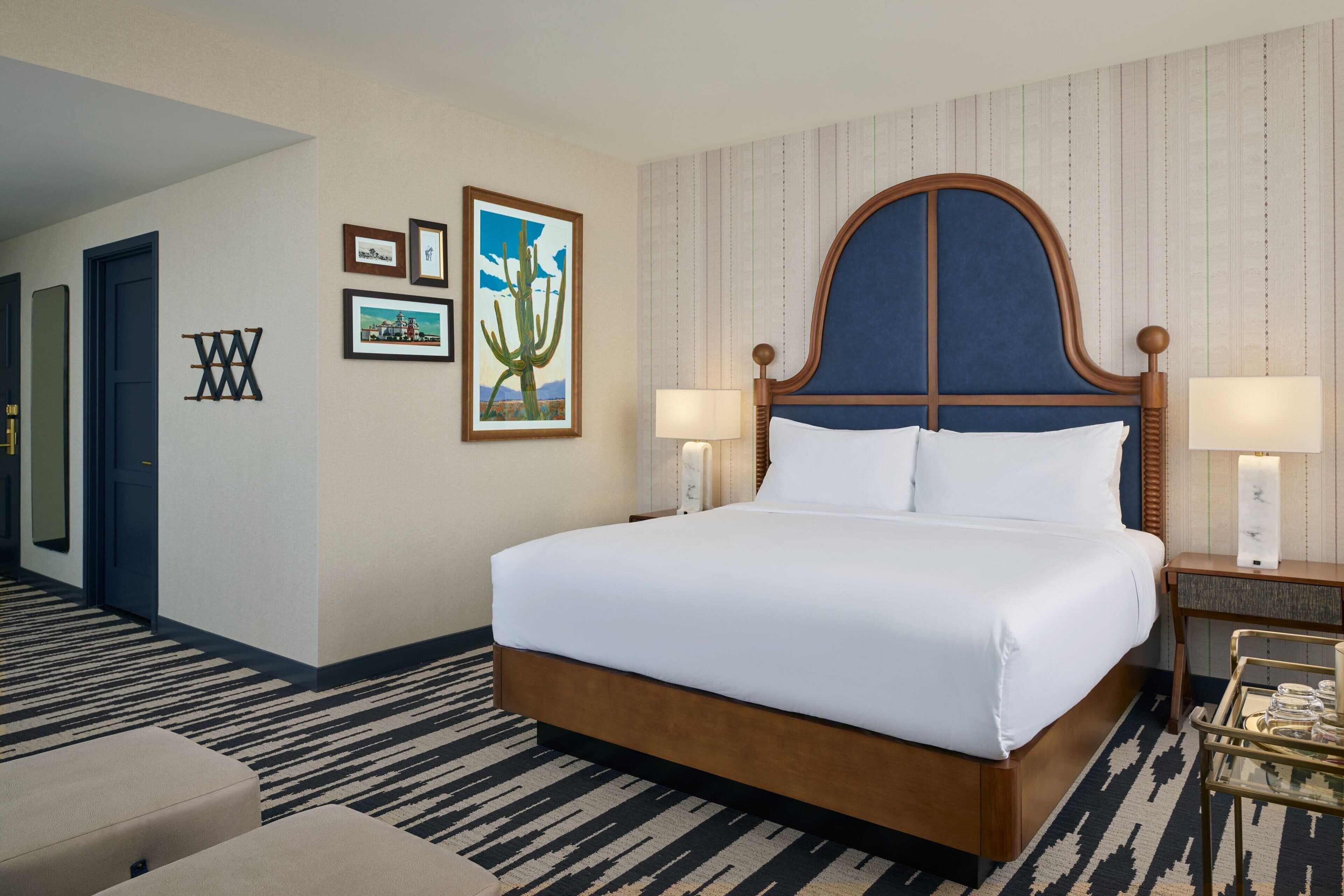 A neatly made bed with a wooden headboard, two bedside lamps, and a small table with a tray of items.