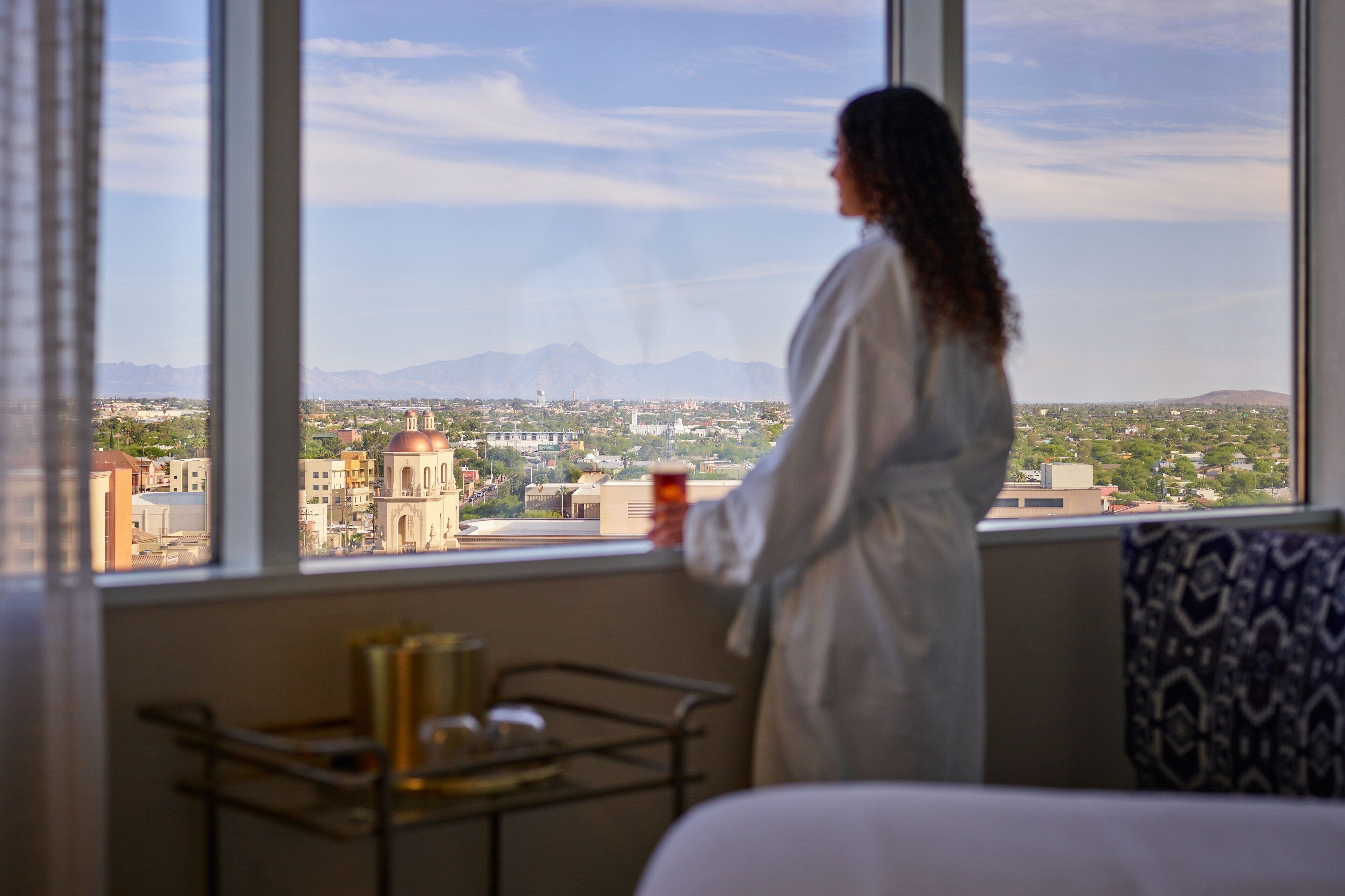 A person standing by a window with a cityscape view, including a prominent building with domes.
