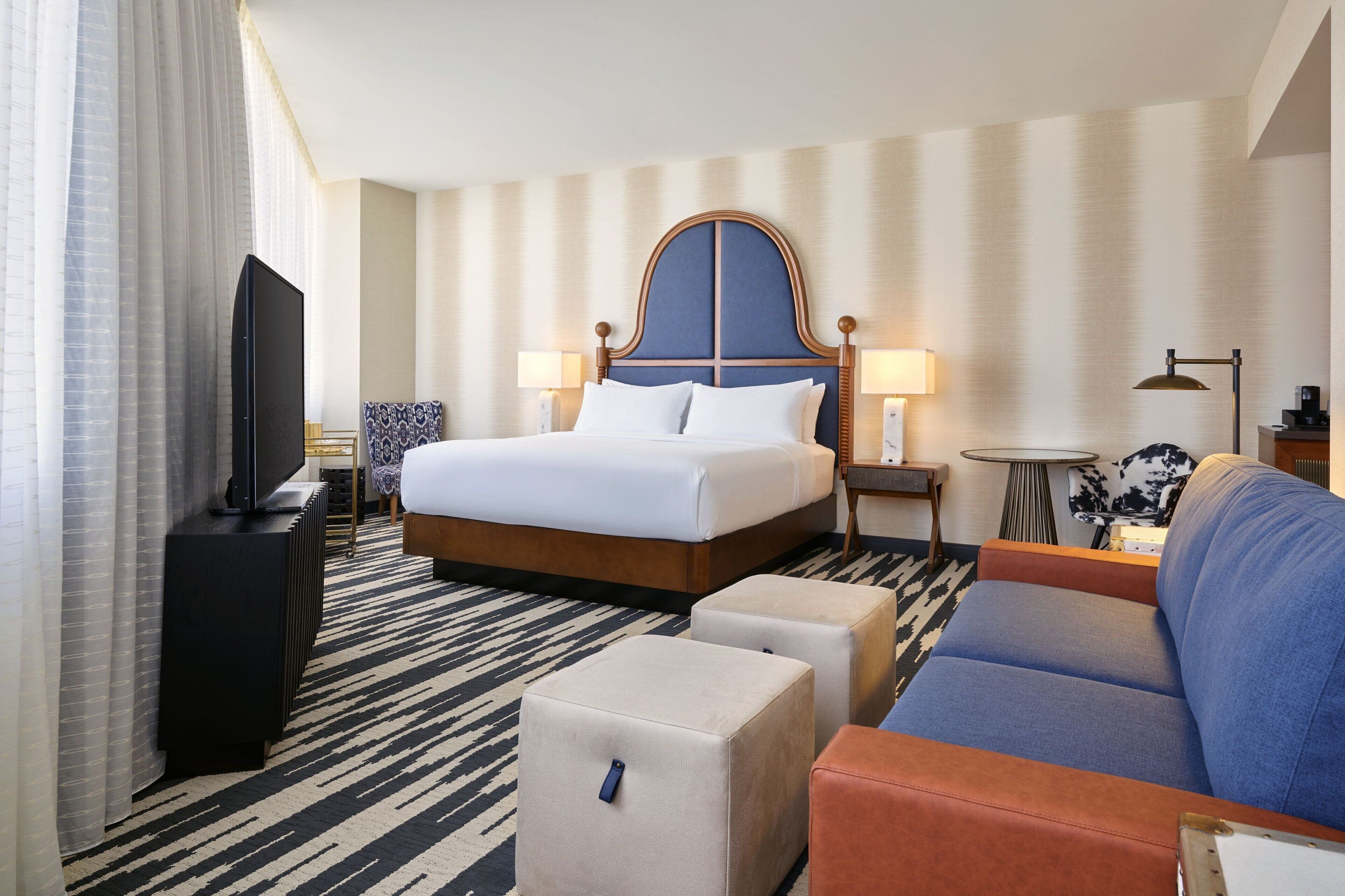 A hotel room with a bed, a sofa, a TV, and a lamp.