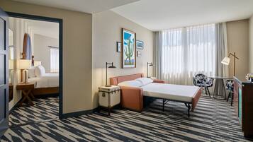 A hotel room with a bed, bedside tables, a desk, a chair, a lamp, a mirror, and a window with curtains.