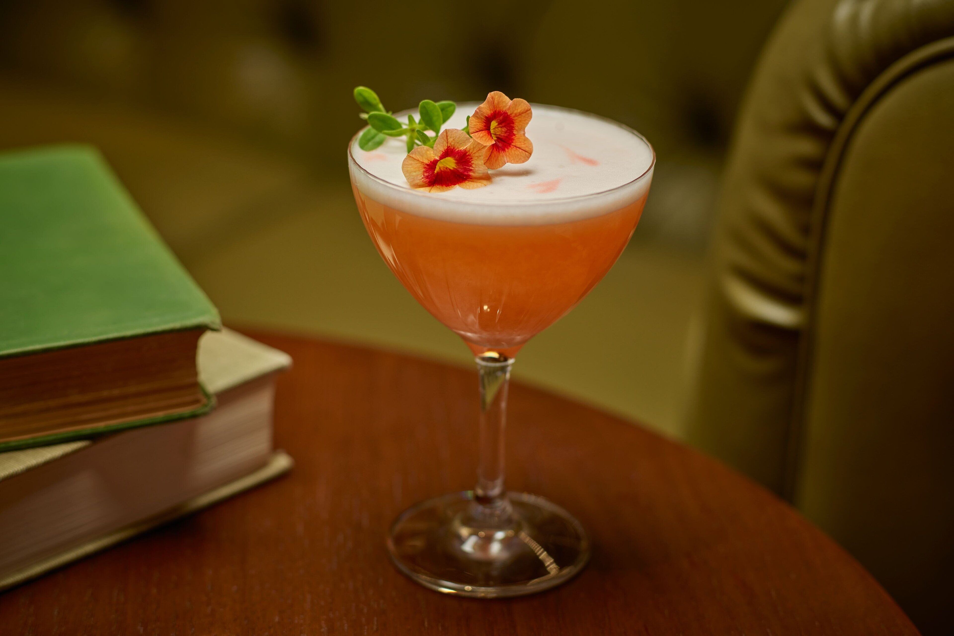 Un cocktail servi dans un verre à martini, agrémenté d’une garniture, sur une table en bois.