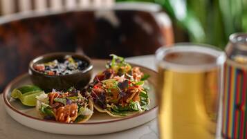 A plate of tacos with a lime wedge, a small bowl of salsa, and a glass of beer on a table.