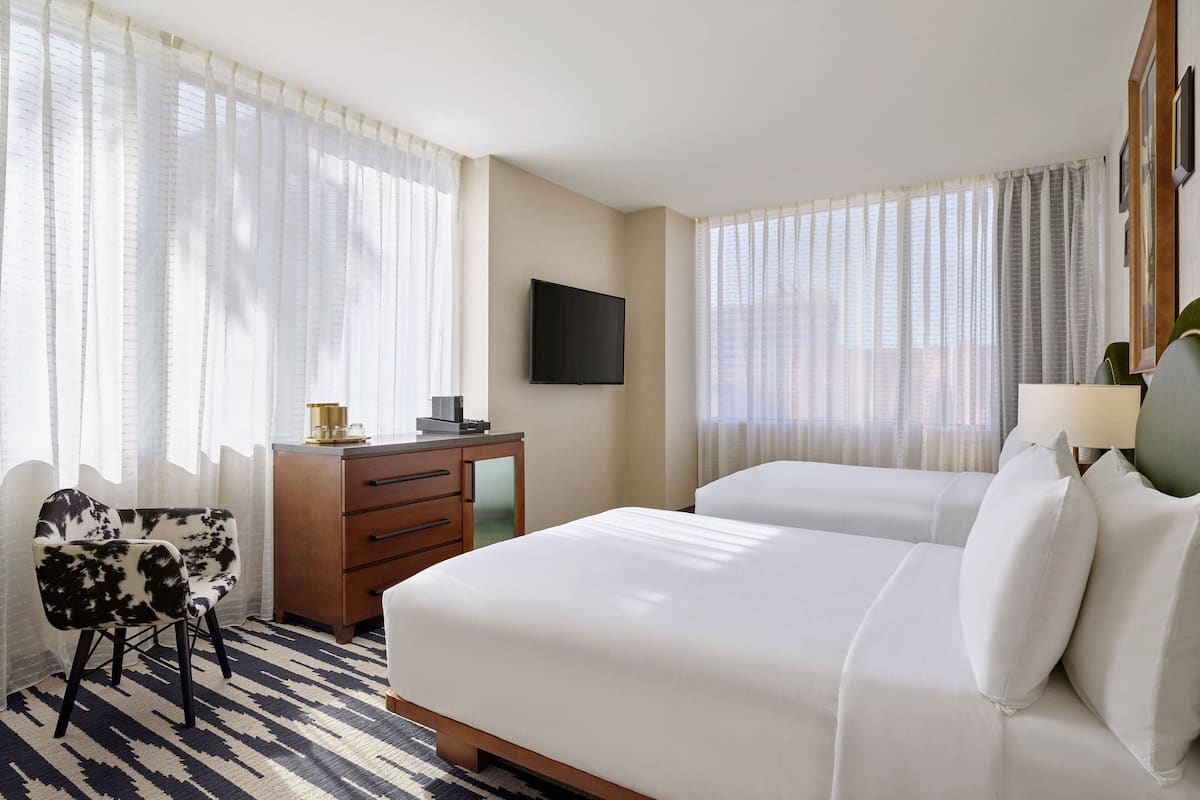 A hotel room with two beds, a desk, a chair, and a TV.